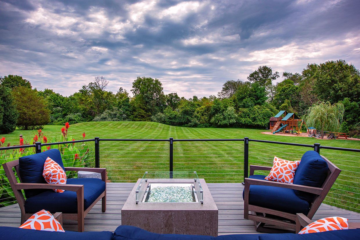 Lounge area with blue cushions and a fire pit on a deck with cable railings.