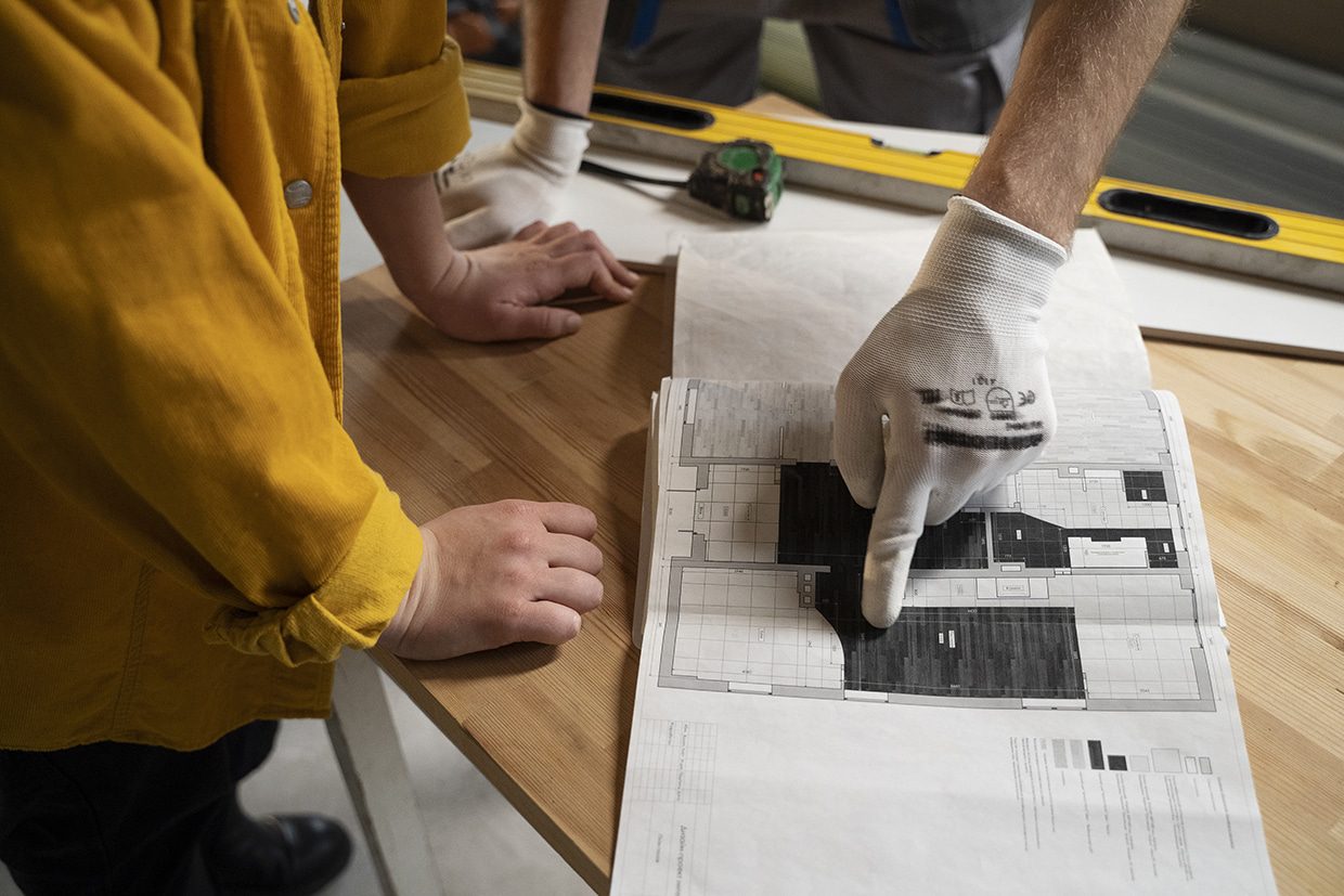 Two builders reviewing architectural blueprints on a table during the backyard deck planning phase.
