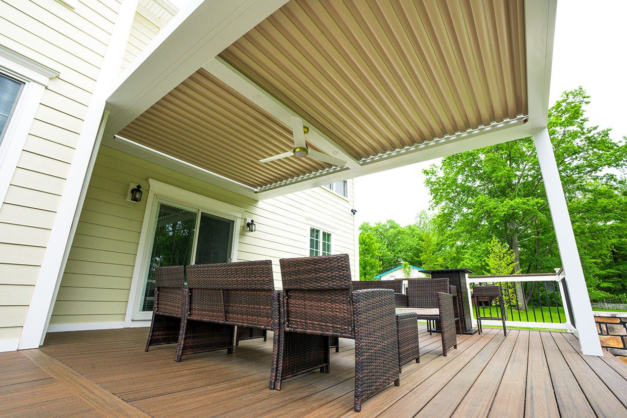 Covered deck with a beige louvered pergola roof and wicker furniture, showcasing functional deck design ideas.