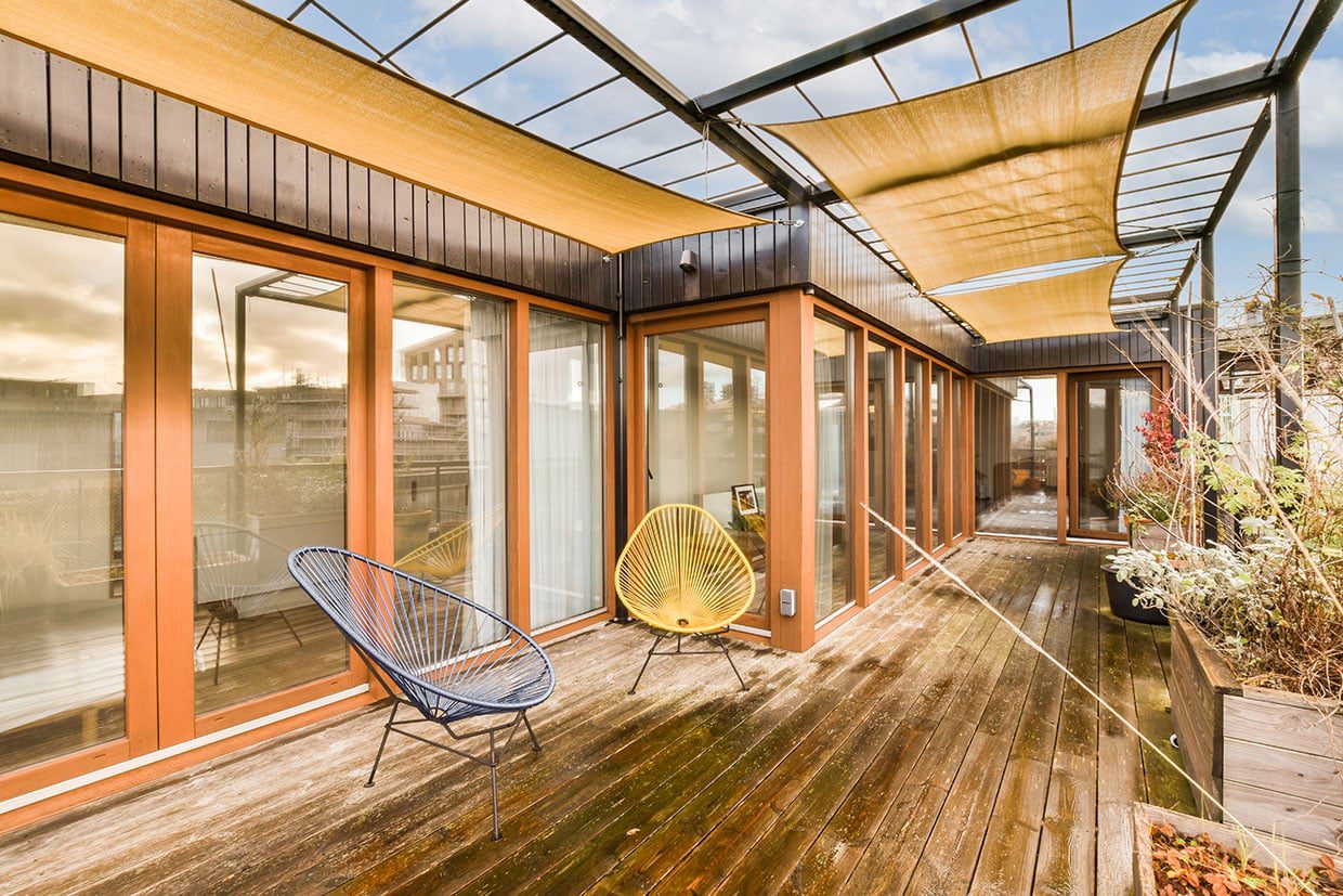 Narrow modern wooden deck with overhead sun shades and yellow Acapulco chairs.