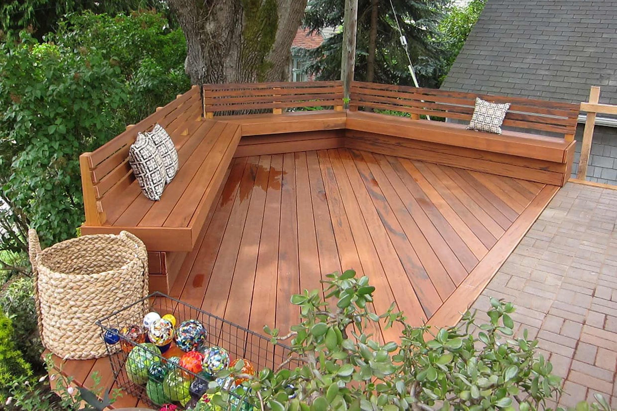 Angular wooden deck featuring built-in bench seating and a tree integrated into the design.