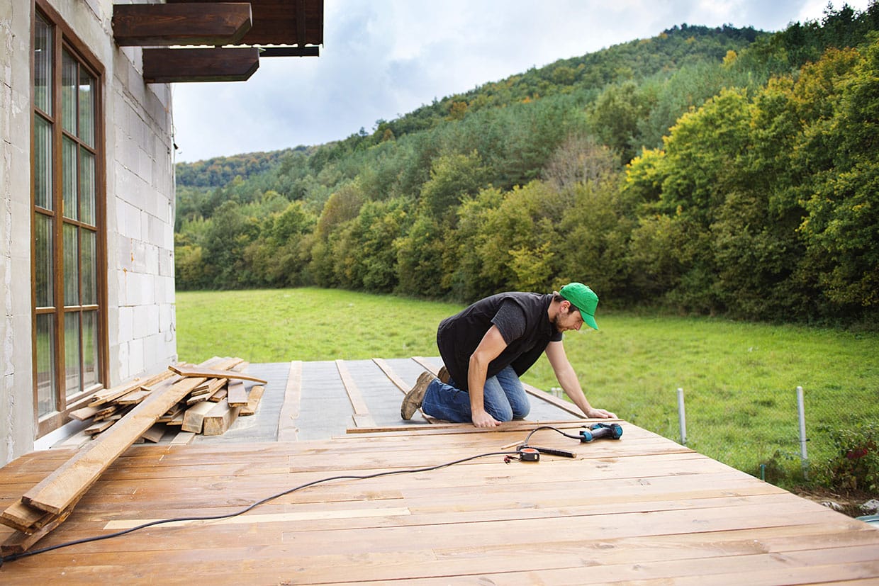 Carpenter installing wooden floorboards on custom decks to create a scenic outdoor area.