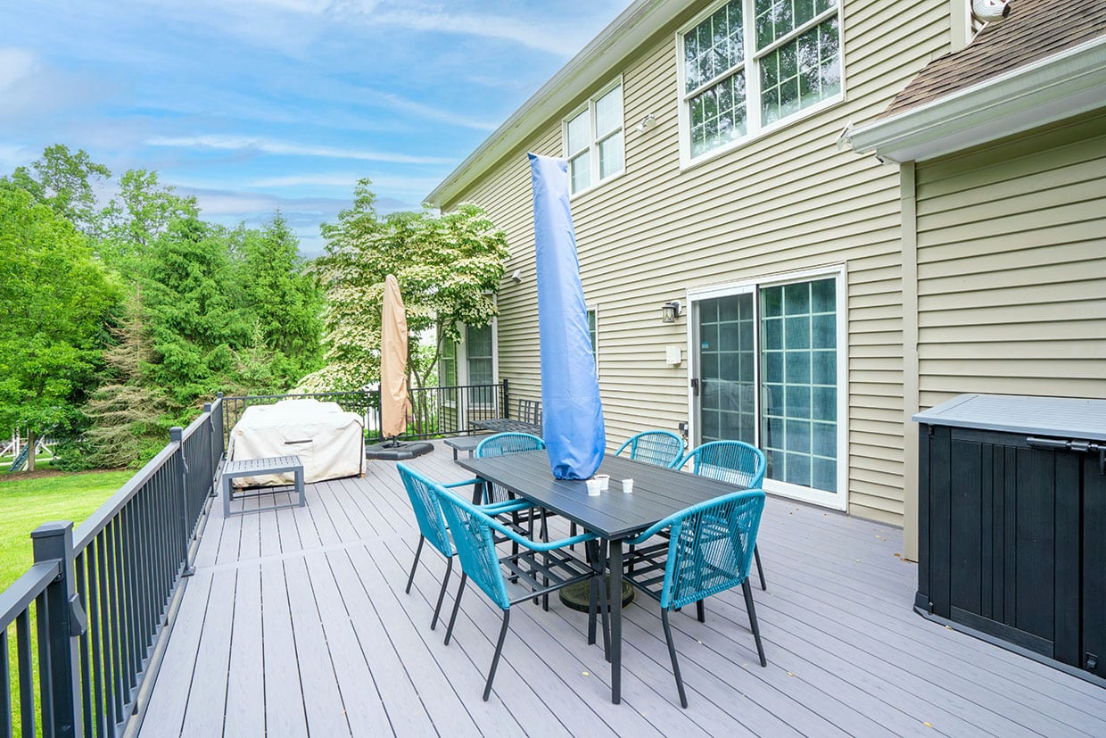 Eye-level view of a grey composite deck with teal dining furniture and sliding door access, showcasing work by a quality Deck Builder in Covington.