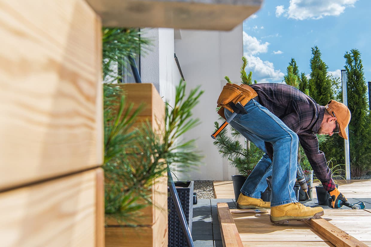 A builder equipped with a tool belt bending over to screw down deck flooring.
