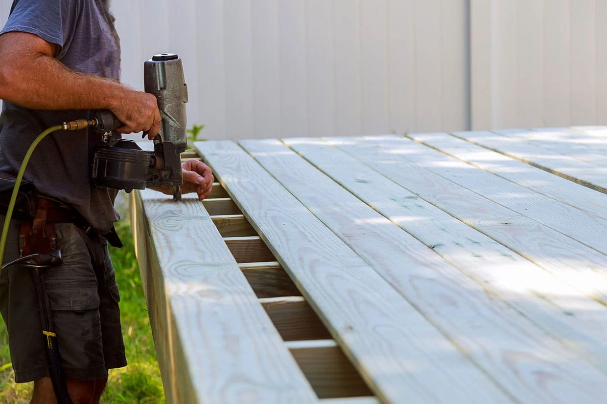 A contractor using a pneumatic nail gun to secure decking boards during installation.
