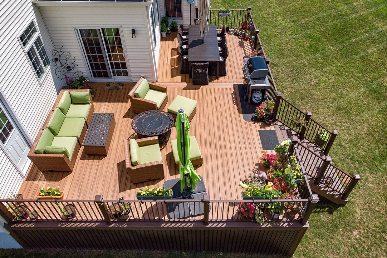 High-angle shot of a tan composite deck furnished with green cushioned wicker furniture and rail planters.