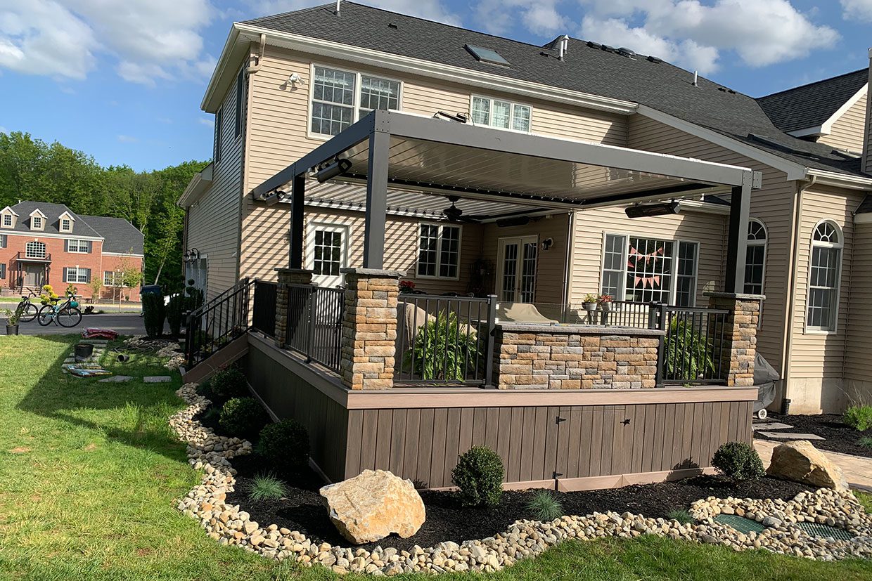 A backyard deck renovation ideas showcase featuring stone-wrapped pillars, an outdoor kitchen, and a large louvered pergola.
