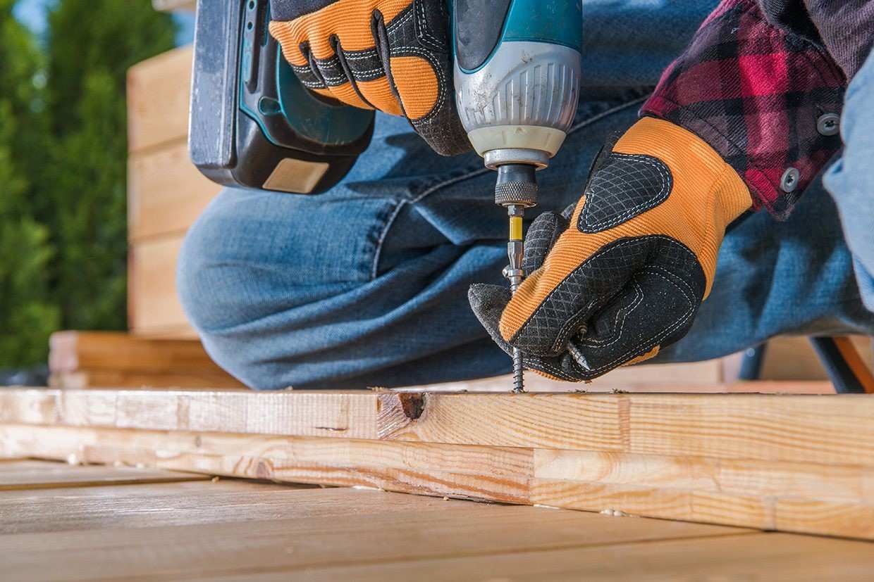 Close-up of hands using a power drill to secure wood planks during a DIY deck restoration.
