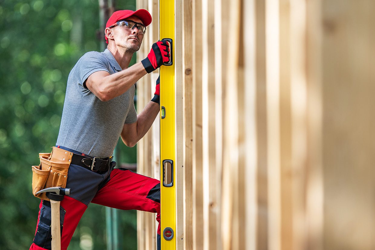 Construction worker using a spirit level to check the vertical alignment of wooden framing.