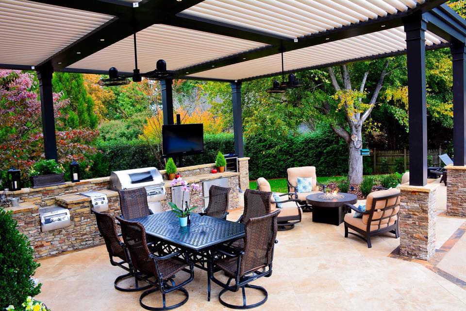 Luxurious patio area featuring a full outdoor kitchen, dining table, and fire pit under a black pergola.