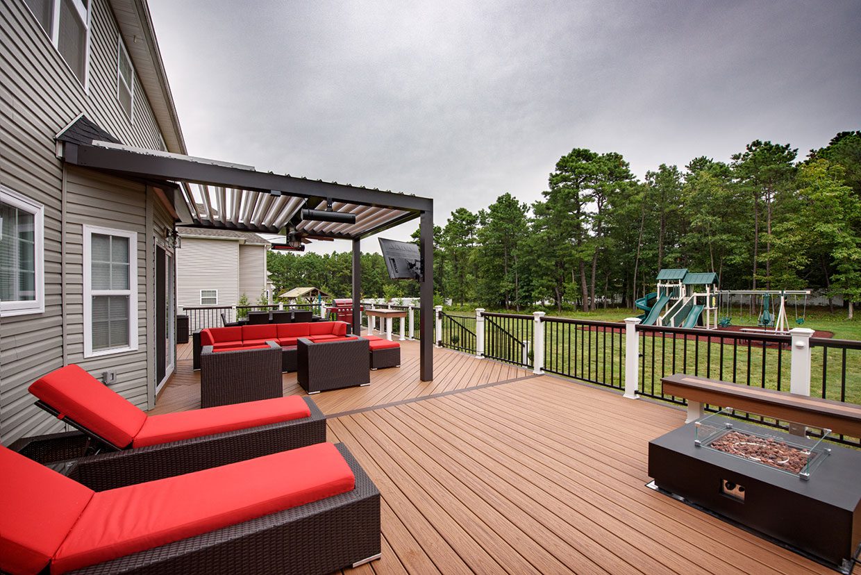 Spacious composite deck featuring red lounge furniture and a modern louvered pergola for shade.