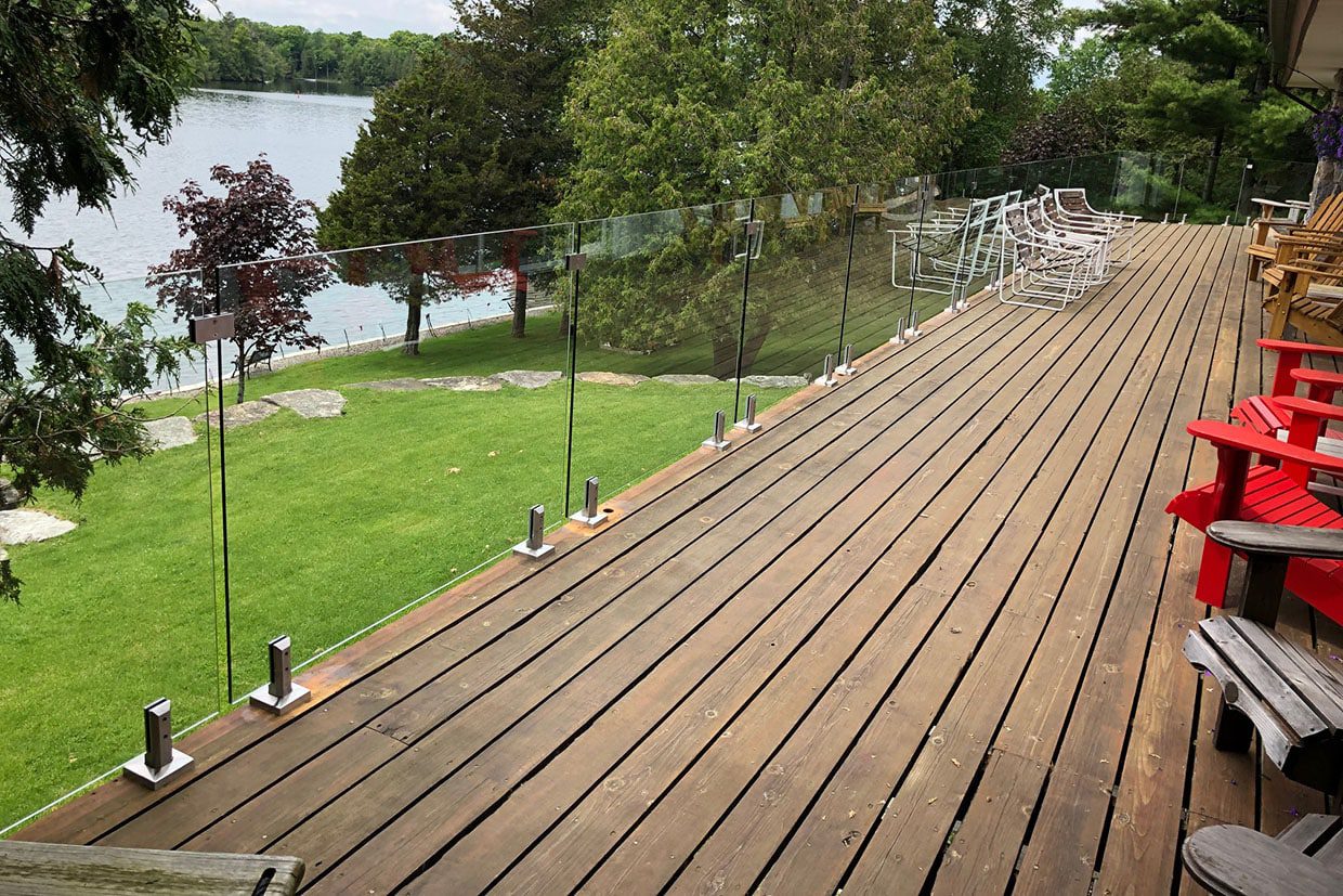 Expansive wooden deck with frameless glass railings representing modern deck styles overlooking a lake.