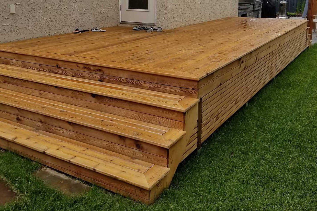 Newly finished wood deck with wide stairs and skirting sitting on a green lawn.