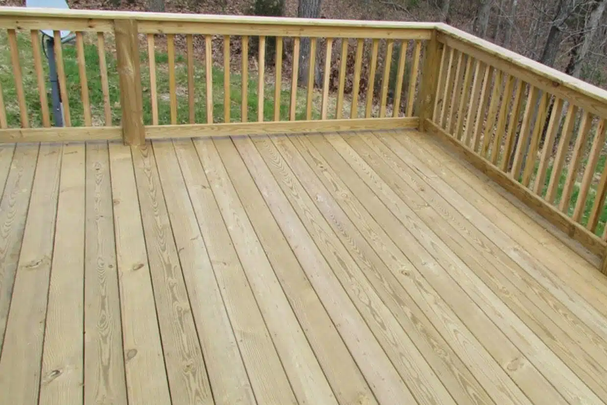 Standard pressure-treated pine deck with a simple vertical railing system overlooking a wooded area.