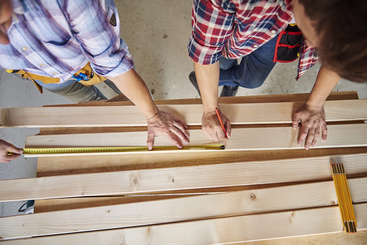 Two professional deck builders measuring and marking wooden planks for precise cutting.