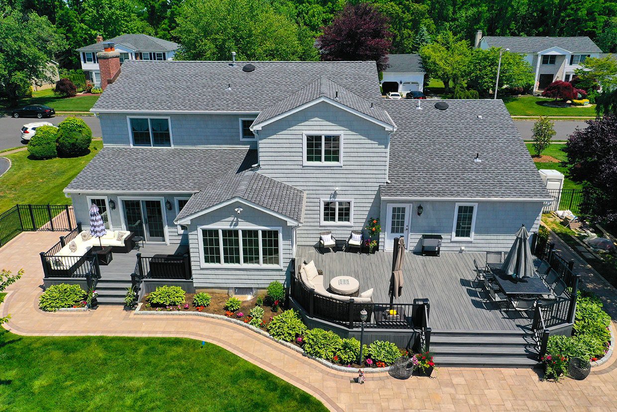 Aerial view of a large gray composite deck with curved railings and a paver patio.