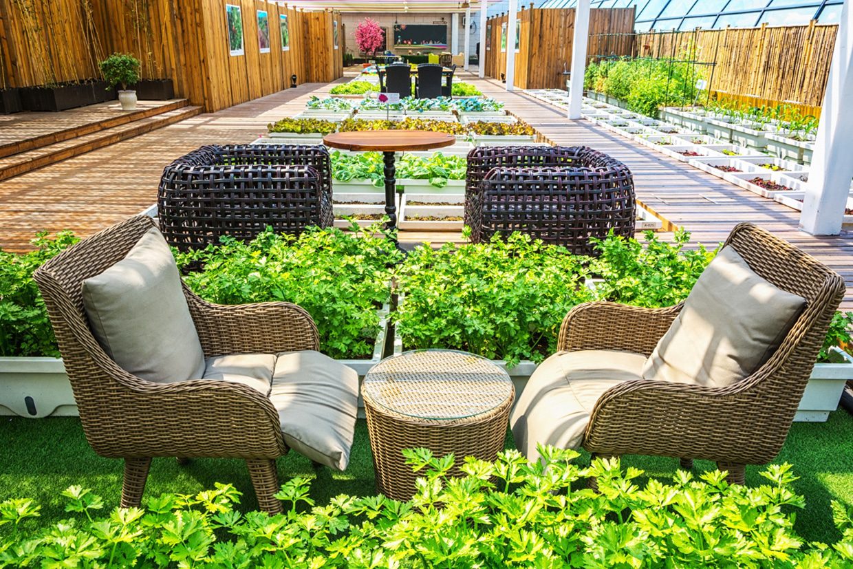 Wicker chairs and a small table sit centrally on a wooden terrace surrounded by rows of white vegetable planters, showcasing functional deck planting ideas.