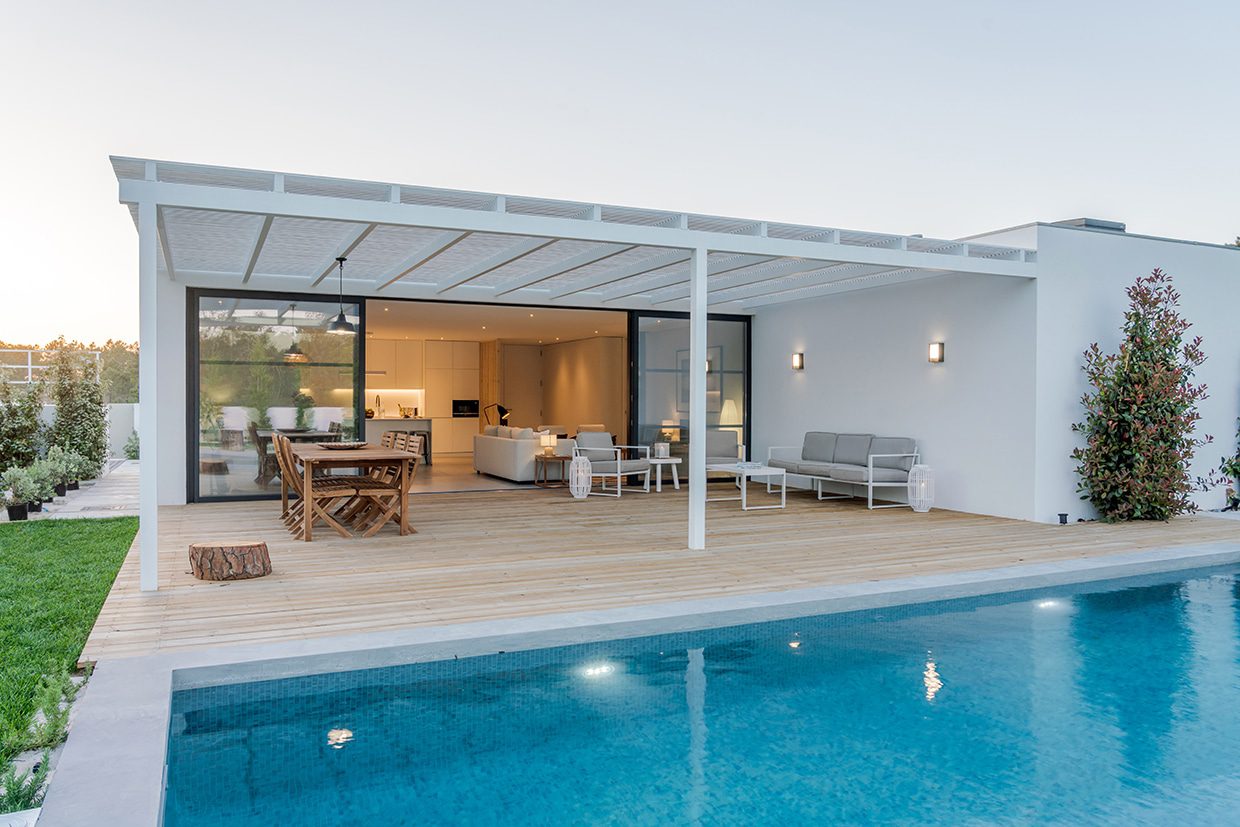 Modern white home featuring a swimming pool and a wooden deck shaded by a white louvered roof system over the lounge area.