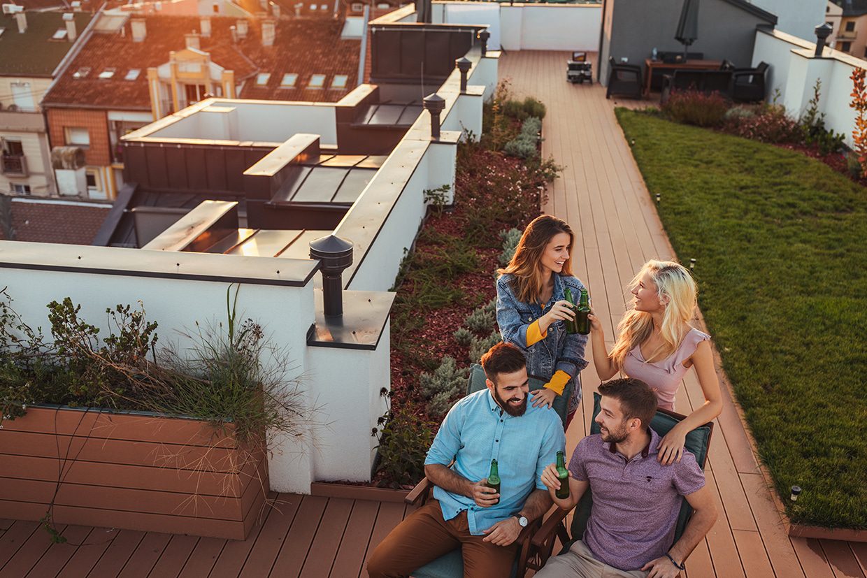 Friends enjoying drinks on a rooftop deck with built-in planters and a city sunset view.