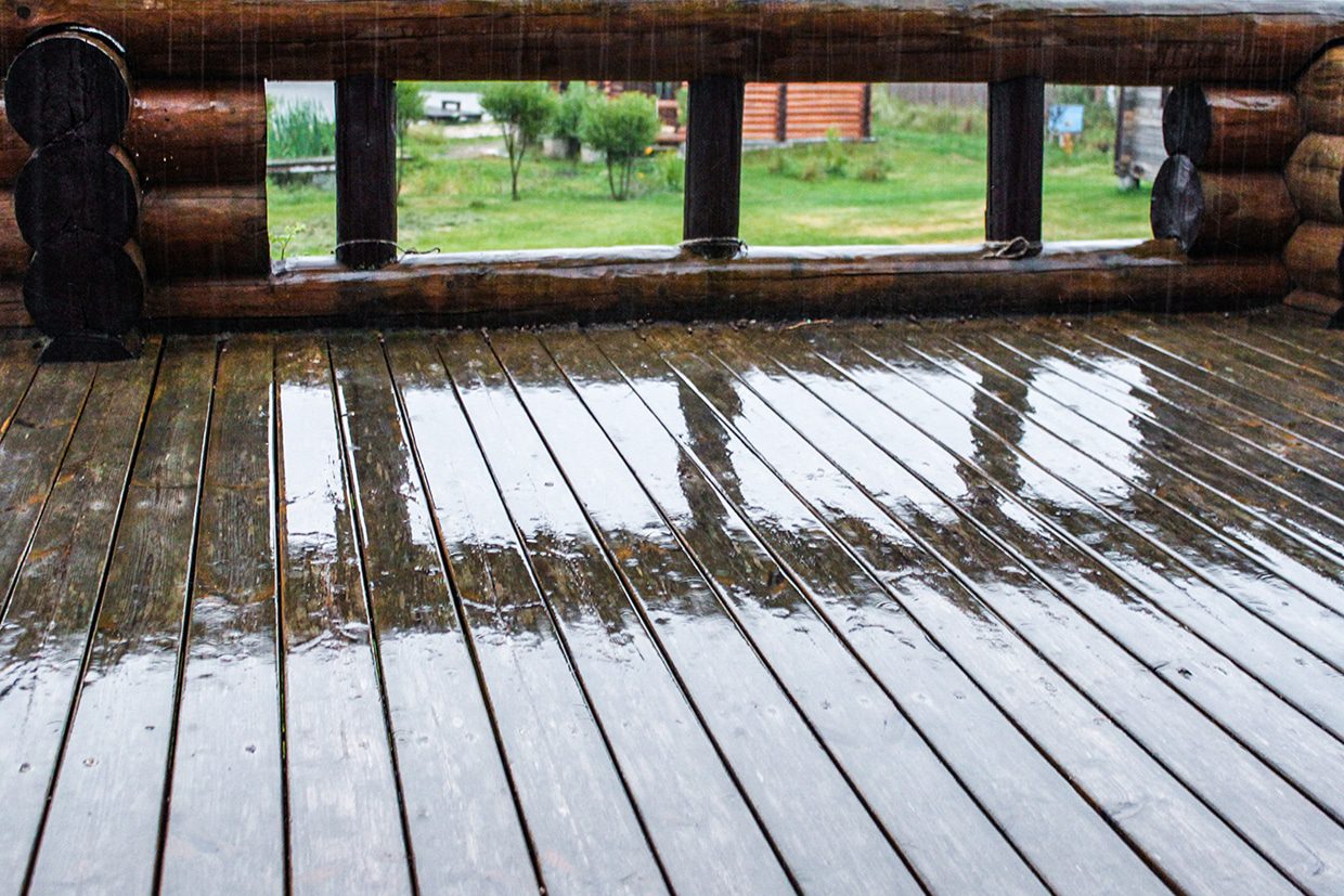 Close-up of rain falling on weatherproof decking boards near a log cabin wall.
