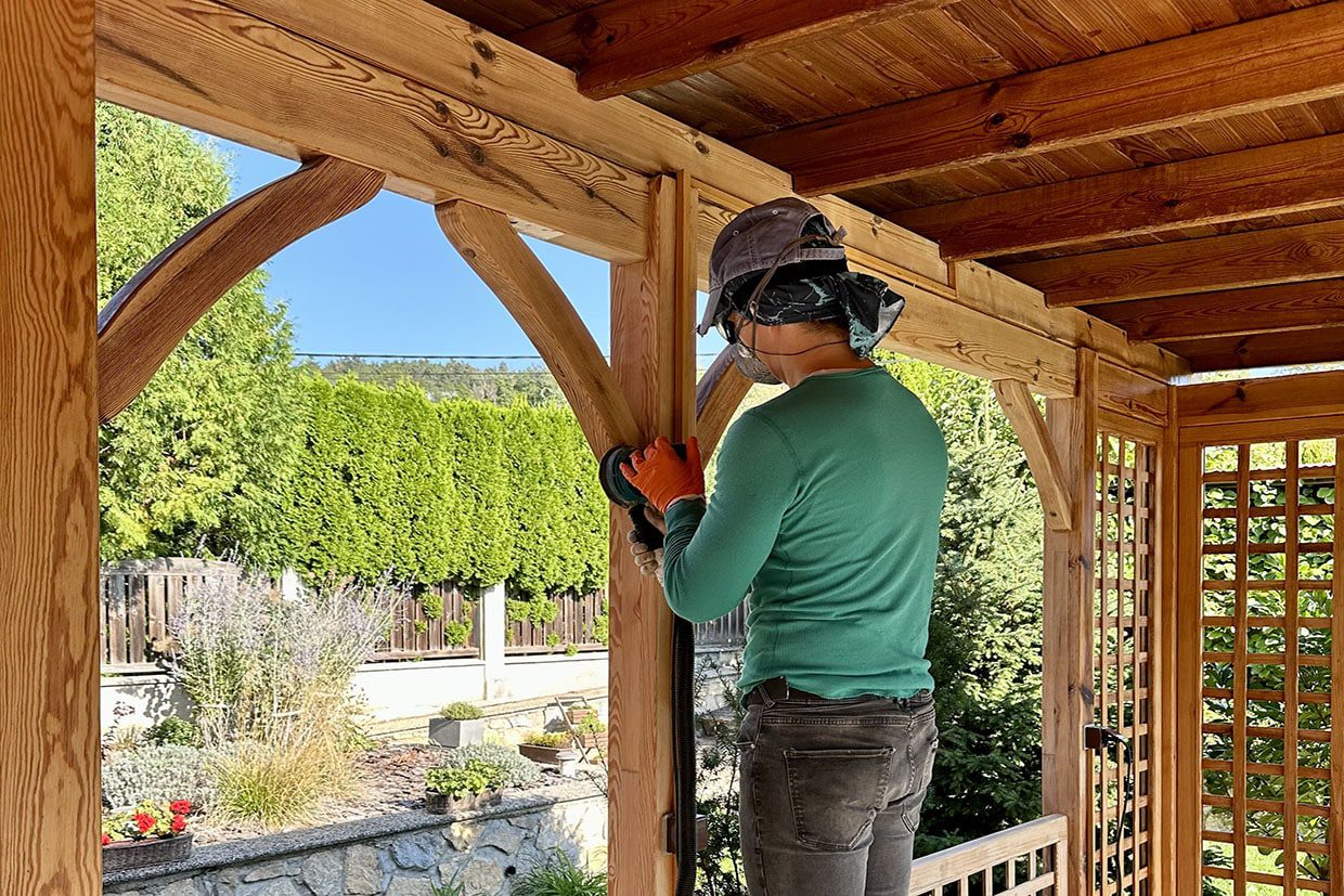 Professional using an electric sander on a wooden beam during a deck resurfacing project.