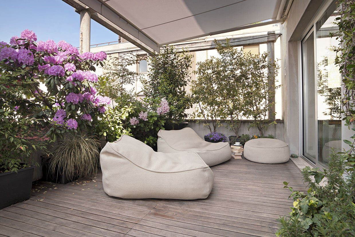 Cozy urban rooftop terrace featuring weathered eco-friendly decking, beige bean bag chairs, and blooming rhododendrons.