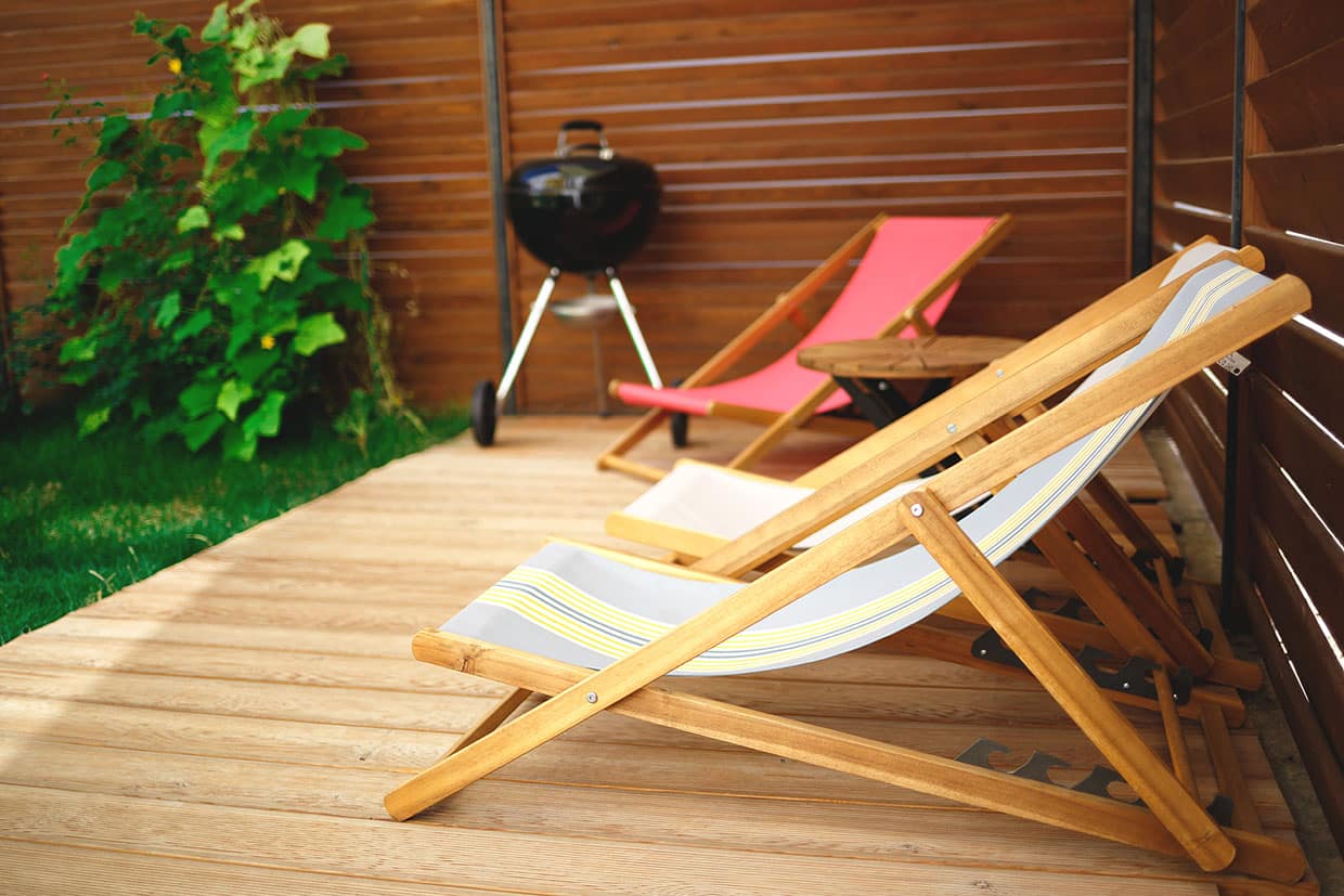 Close-up of a sunny patio area with light-colored bamboo decking, canvas folding chairs, and a wooden privacy screen.