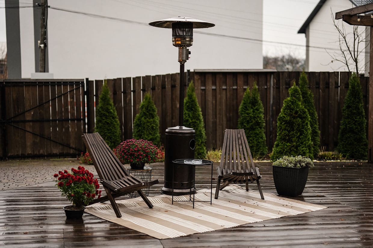 Tall patio heater standing between two wooden chairs on a wet deck, showcasing weather-resistant materials and smart deck features for year-round comfort.