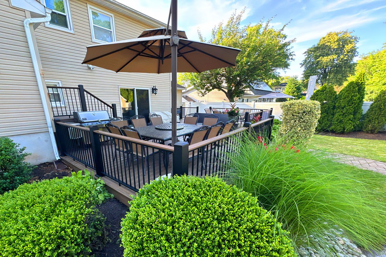A furnished outdoor living space featuring a dining table with an umbrella, grill, and black metal railings, offering backyard deck inspiration for family gatherings.