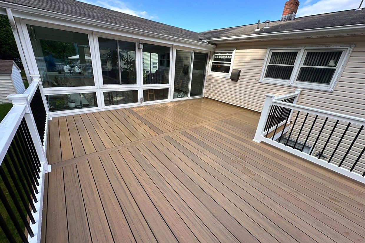 Expansive multi-level brown composite deck with black railings attached to a beige home with a sunroom.