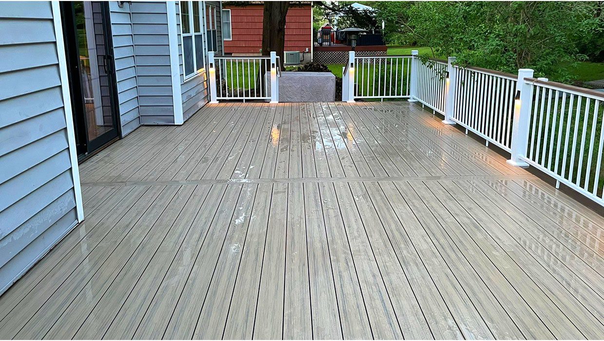 A wide, wet grey composite deck surface showing wood grain texture, bordered by white railings, illustrating a versatile deck design for home style enhancements.