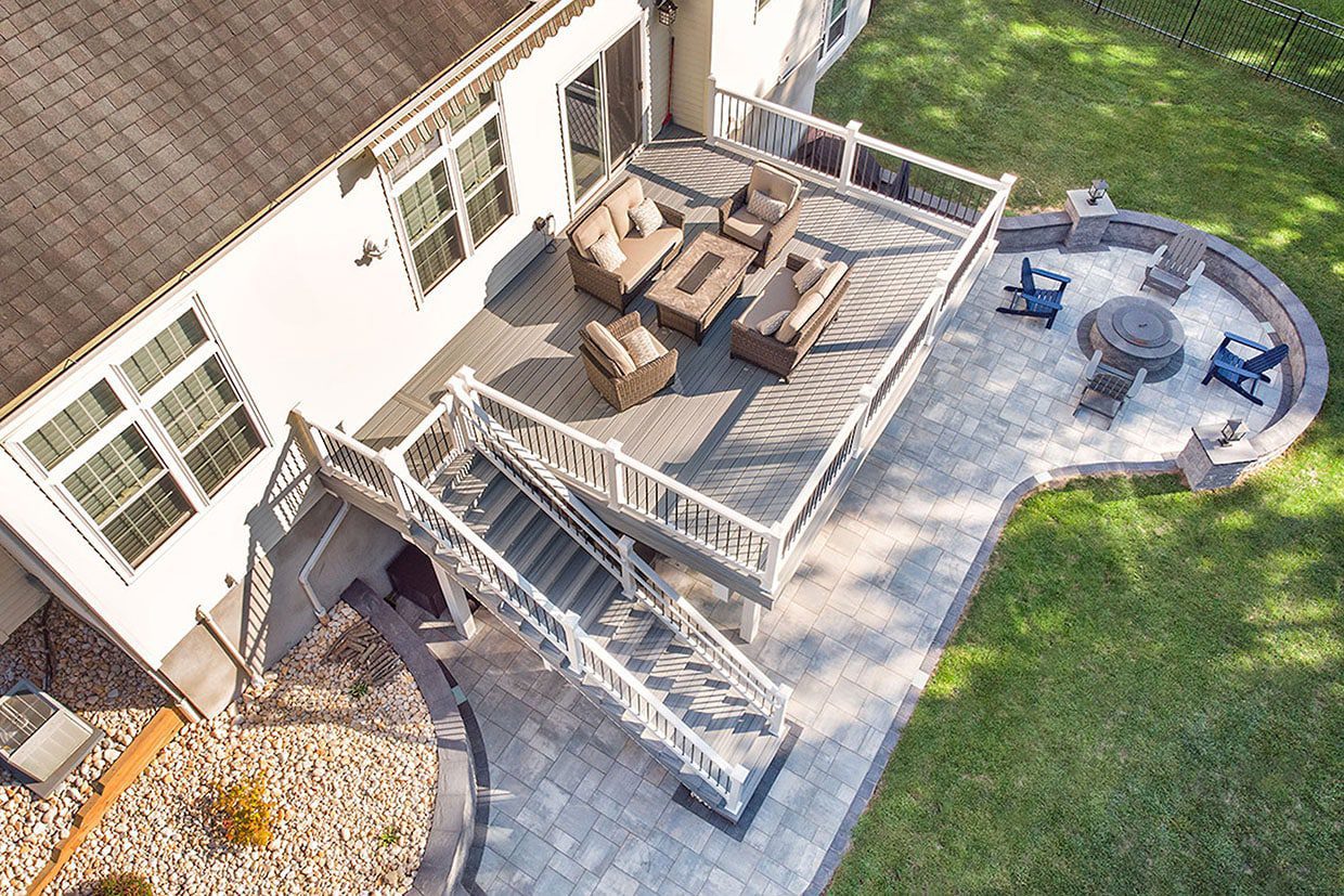 Gray composite deck with a wide staircase leading down to a curved paver patio with a fire pit.