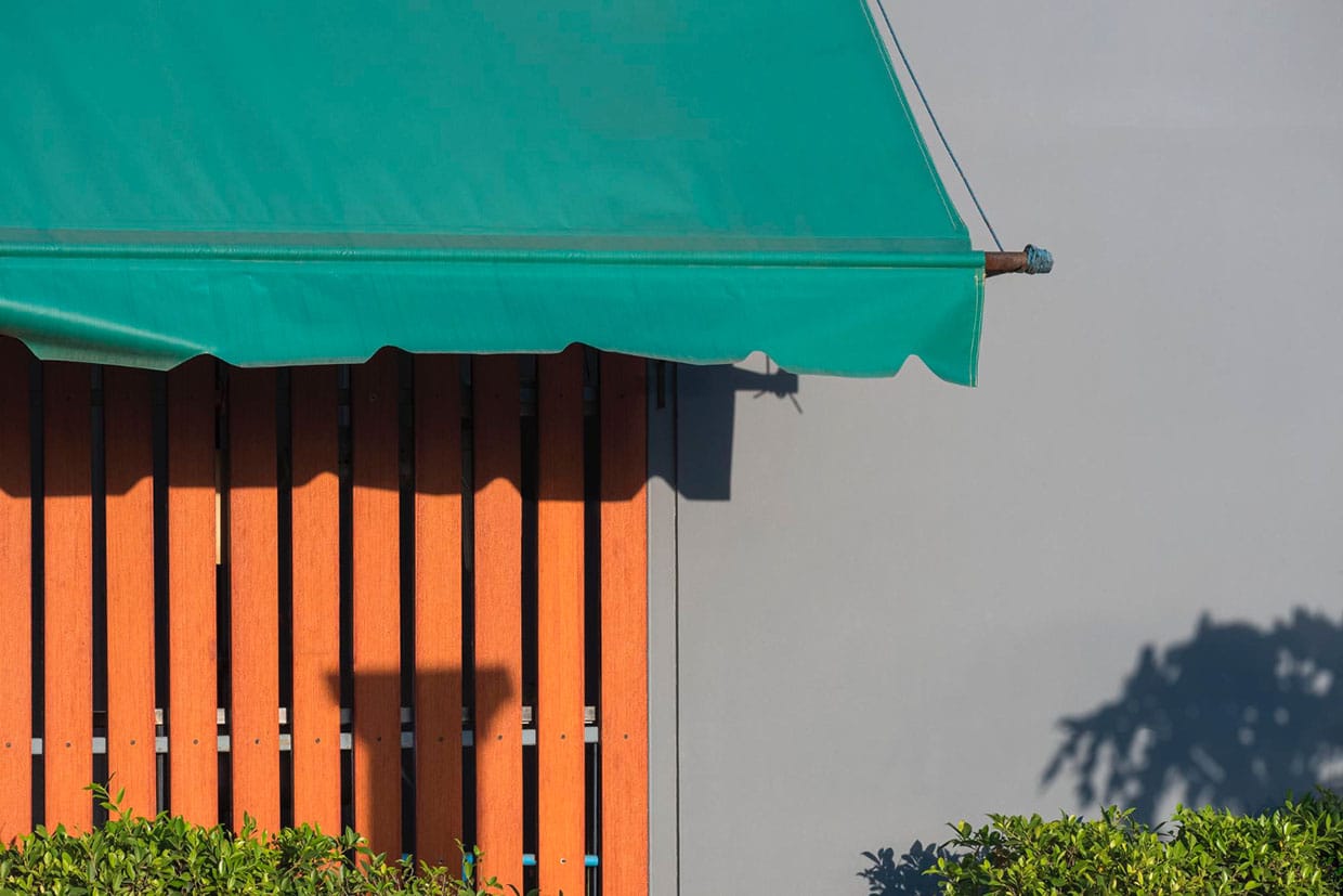 A close-up of a vibrant green canvas awning projecting over a vertical wooden slat wall, creating shade and contrasting textures for outdoor awning ideas.