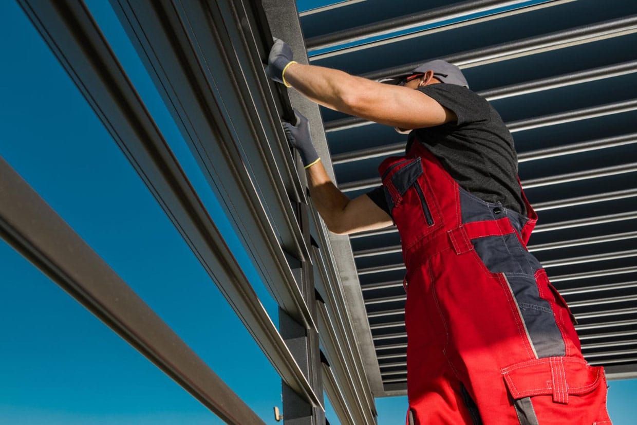 A professional installer adjusts the louvers of a robust metal deck awning, demonstrating the precision and durability of modern pergola-style awnings.