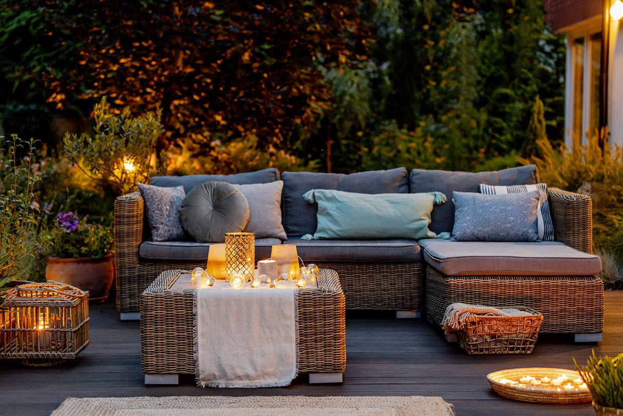 Outdoor wicker sofa and table set styled with cozy pillows, candles, and outdoor string lights as part of seasonal deck decor.