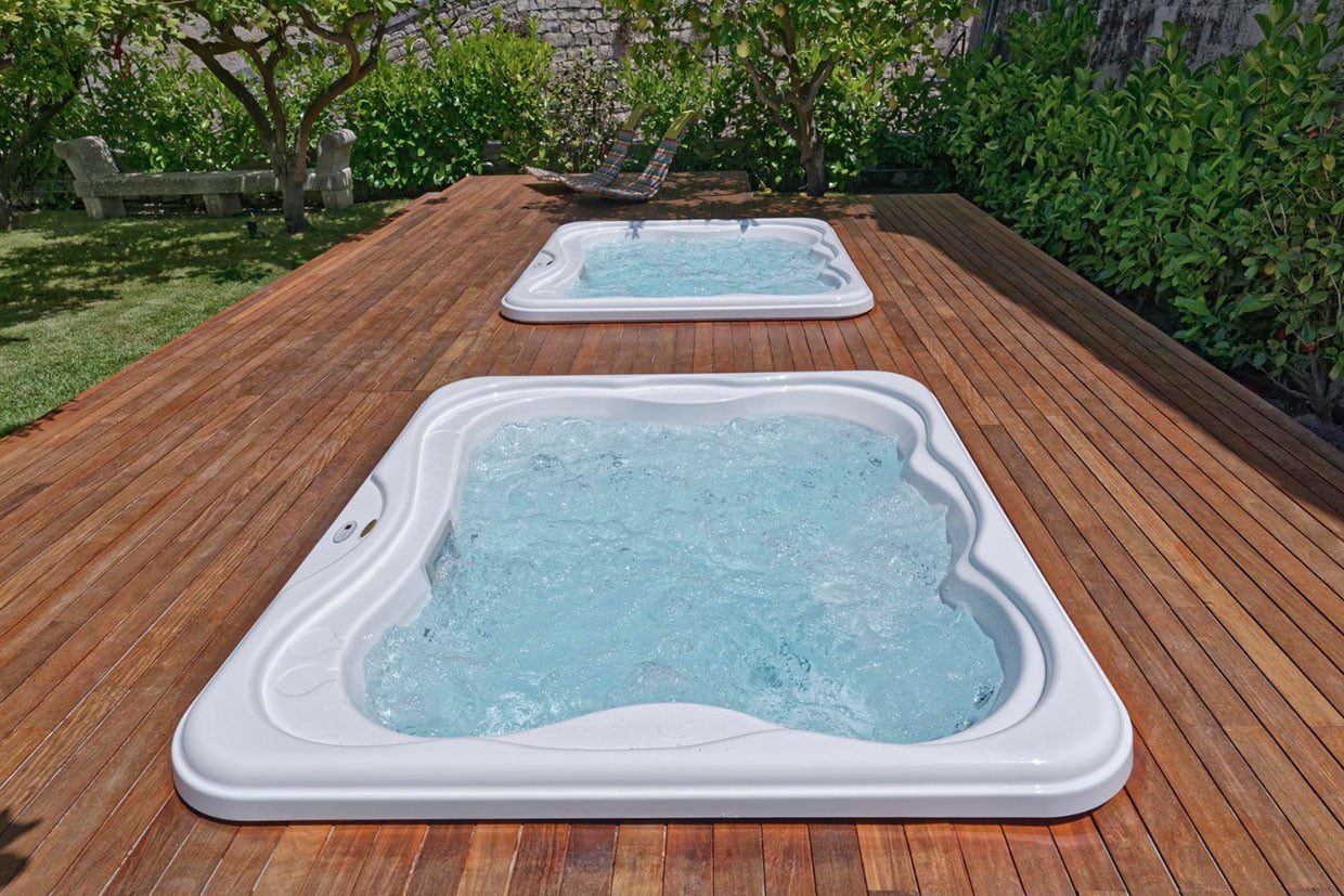 Two rectangular spas recessed flush into a expansive hardwood deck, showcasing a seamless integrated hot tub deck design surrounded by greenery.
