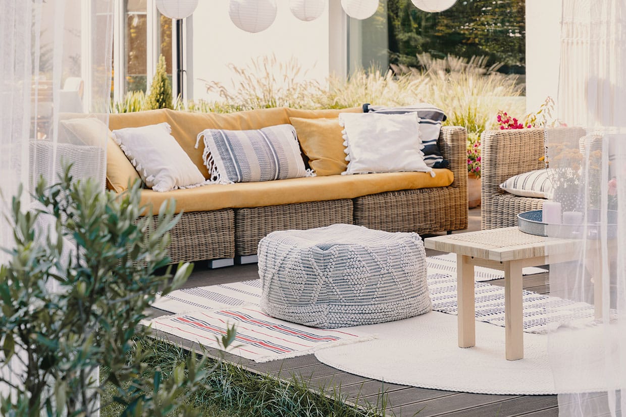 Wicker outdoor sofa with yellow cushions and textured rugs styled under hanging paper lanterns for summer deck decorations.