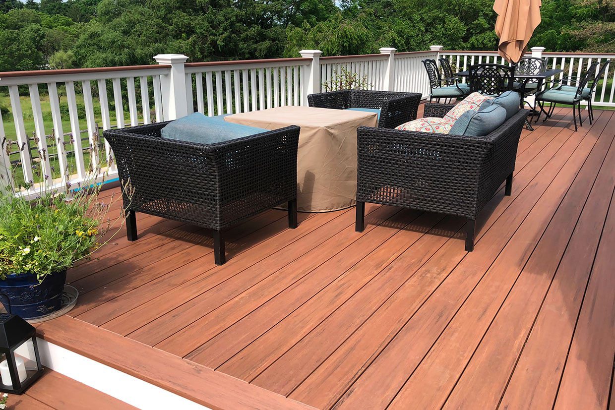 A spacious outdoor deck built with sustainable deck materials, featuring rich brown composite boards, black wicker furniture, and white railings.