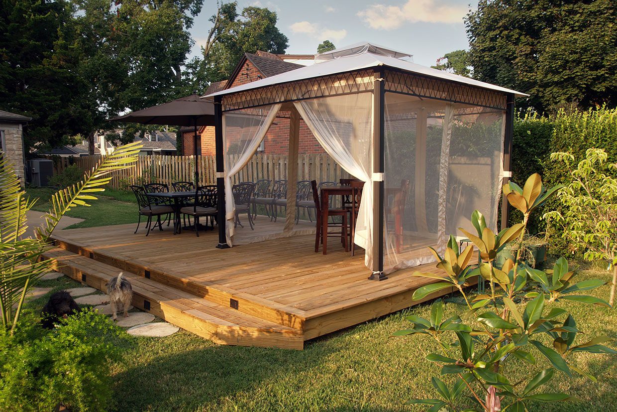 A spacious backyard deck idea featuring a large wooden platform supporting a screened gazebo and dining set.