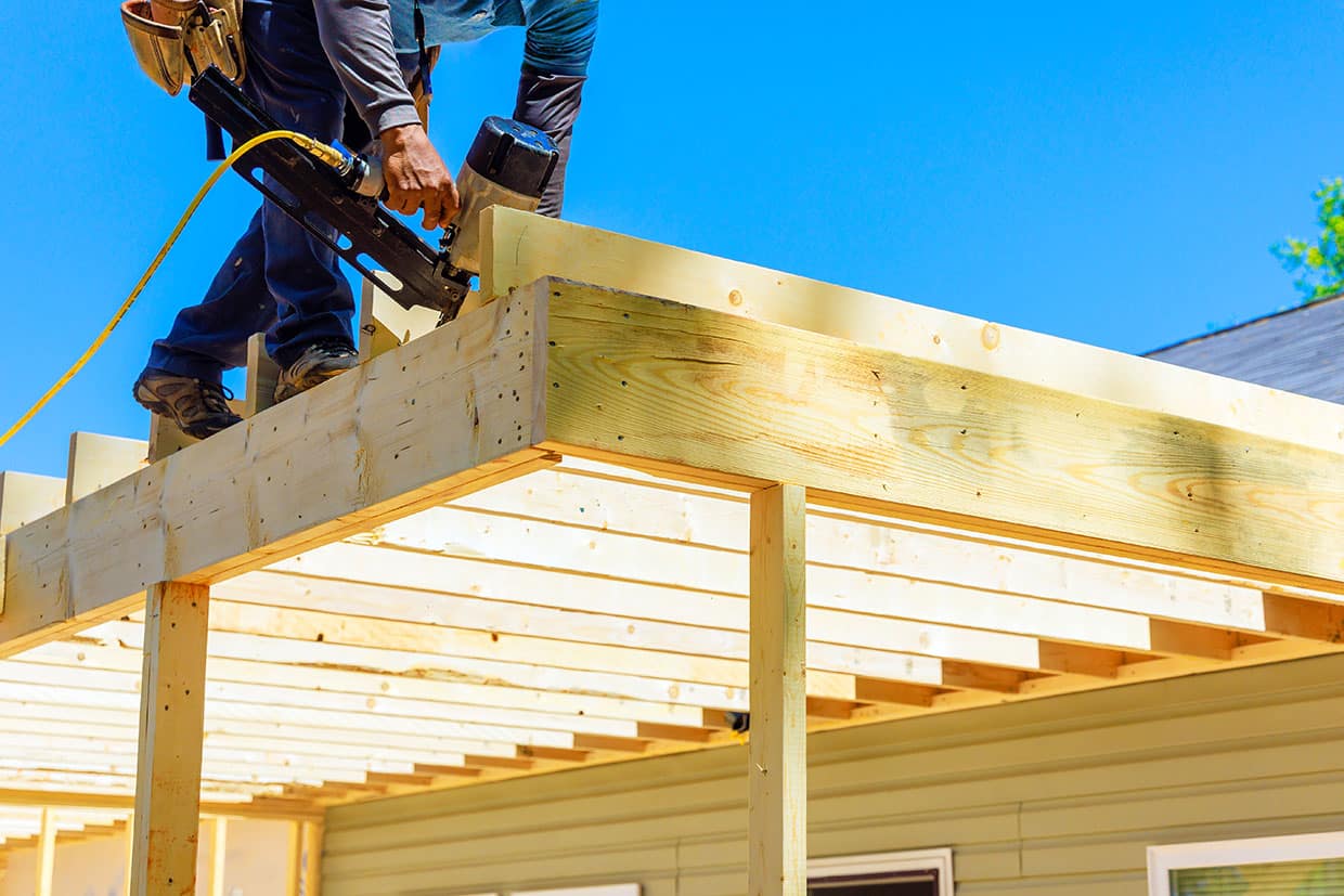 How to Build a Deck Builder using a pneumatic nail gun to secure wooden joists, demonstrating the framing phase of how to build a deck.