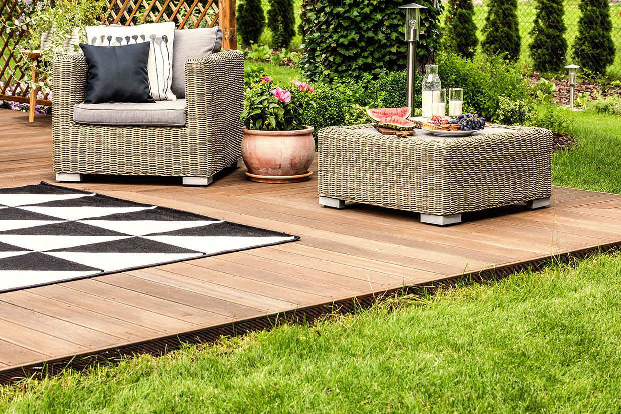 A cozy outdoor living space styled with wicker armchairs, a table, and a rug on a low-profile wooden surface.