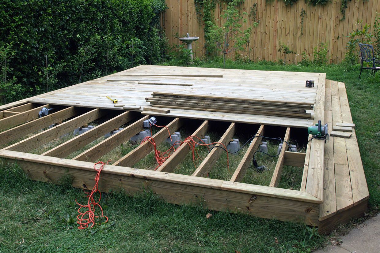 Work-in-progress shot showing how to build a floating deck with exposed joists, concrete blocks, and stacked decking boards.