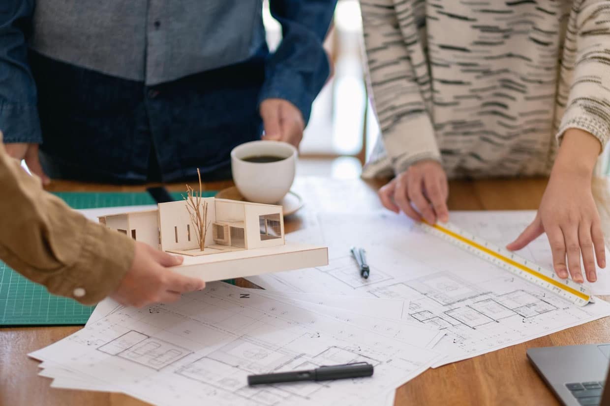 How to Build a Deck Team reviewing architectural blueprints and a house model to finalize backyard deck plans.