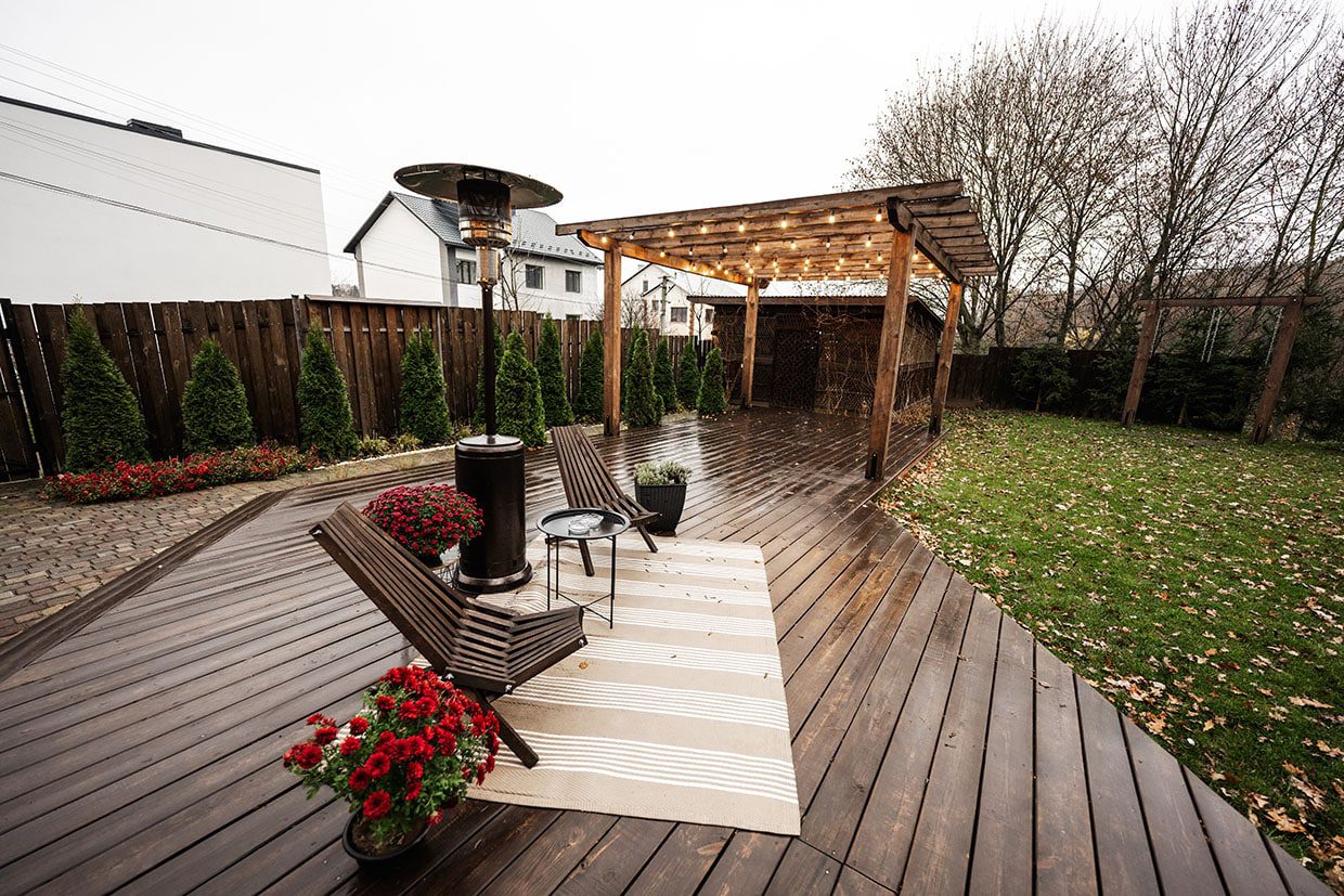 A stylish, dark-stained ground level deck equipped with a pergola, string lights, and a patio heater for cold weather.