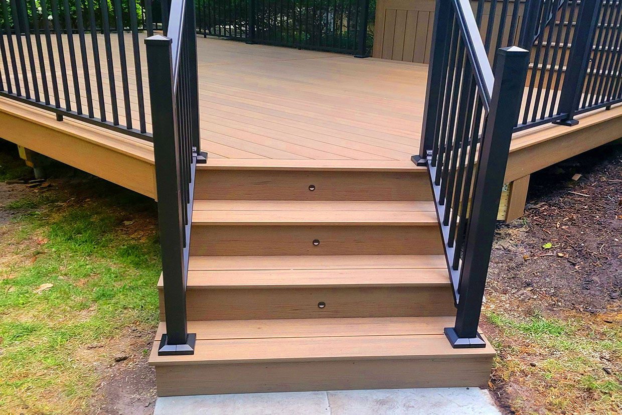 Close-up of modern composite deck stairs featuring integrated riser lights and black metal railings for safety.