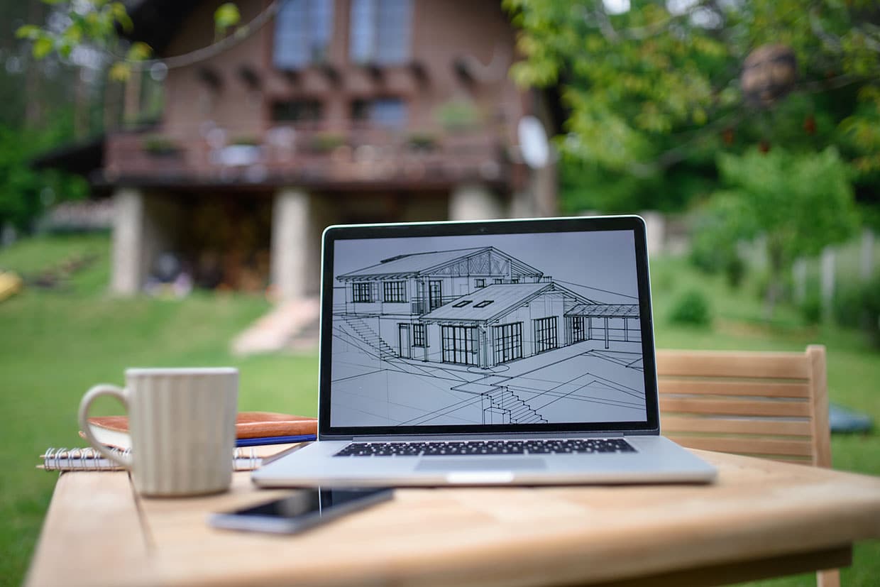 Laptop displaying a wireframe architectural sketch of a house and deck sitting on an outdoor wooden table.