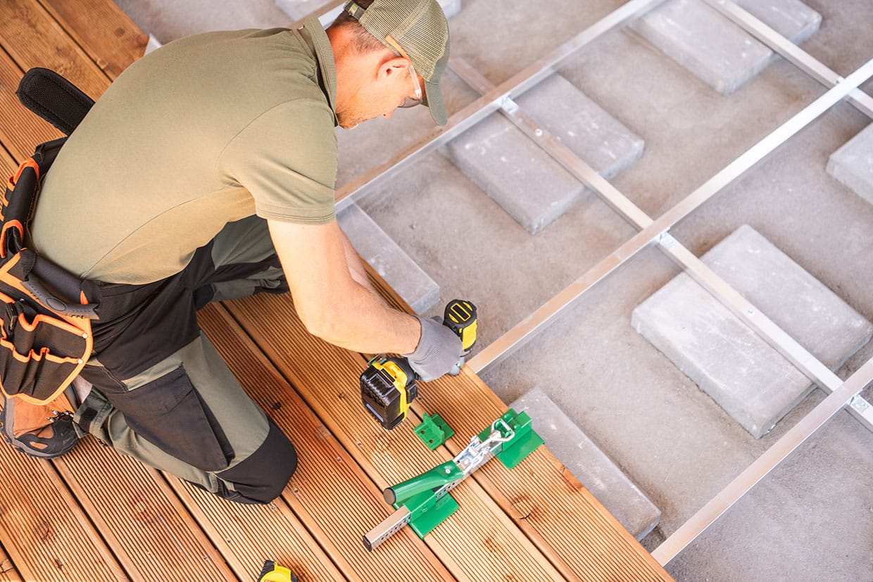A construction worker using a power drill and a hidden fastener tool to secure decking boards onto a metal substructure.