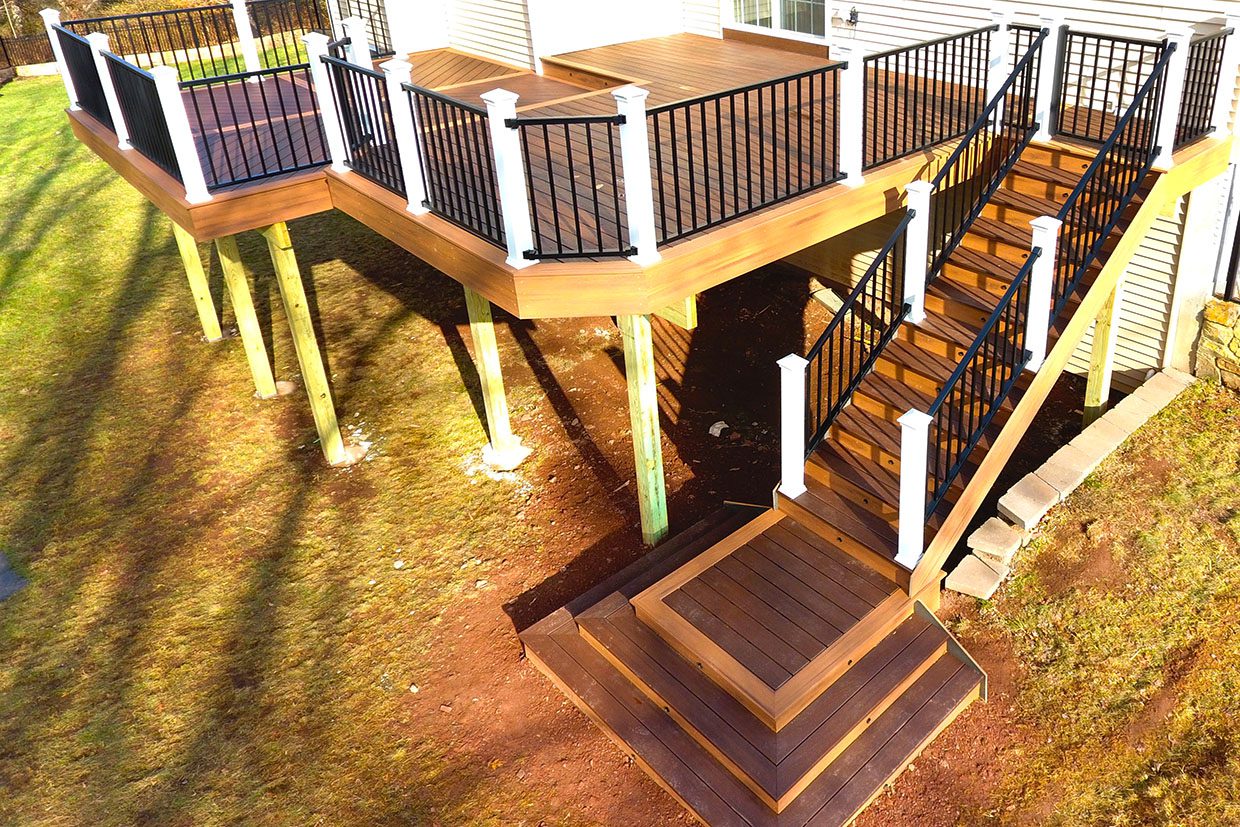 Aerial view showing the structural components of how to build deck stairs for high elevations, including pressure-treated wood stringers, landings, and white railings.
