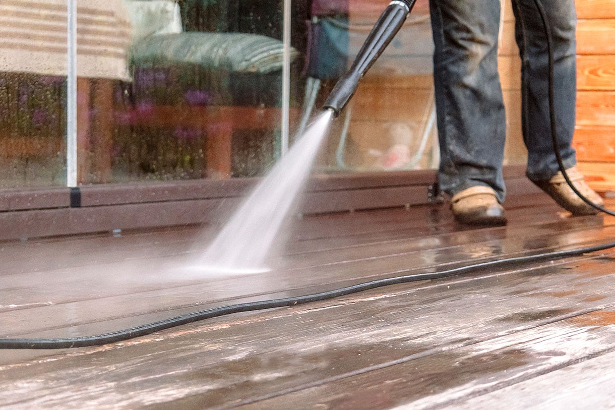 Person using a spray wand to wash the floor, demonstrating how to clean composite decking efficiently.