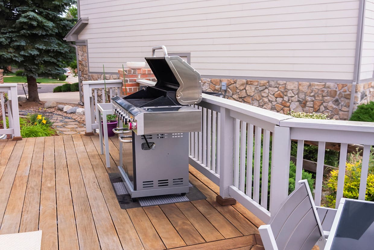 A stainless steel gas grill positioned on a dry composite deck with a protective mat underneath.
